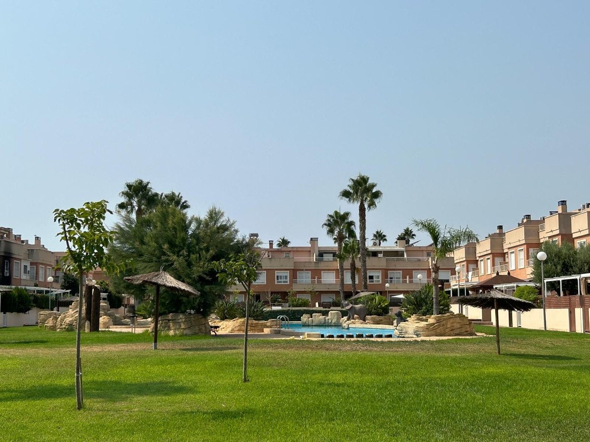 Townhouses with a swimming pool, palm trees, and lush green lawn in a sunny outdoor area.