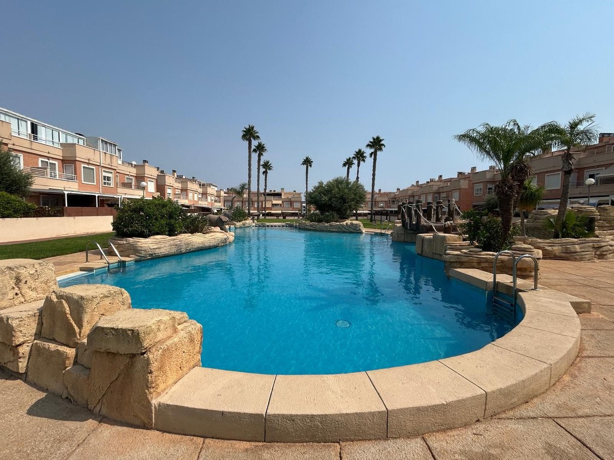 A large, bright blue swimming pool with artificial rock features and palm trees, adjacent to residential buildings.