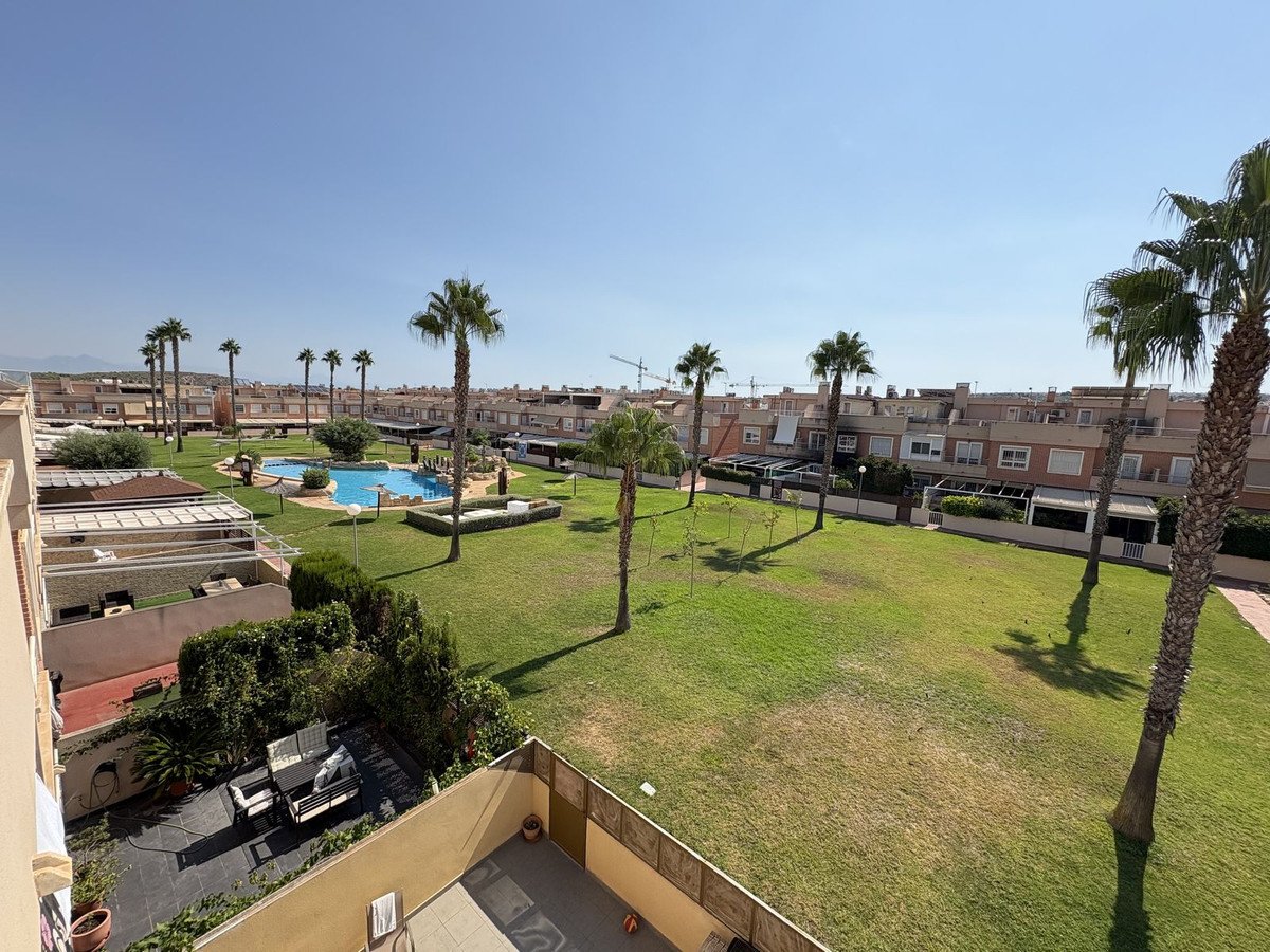 A view of a residential complex with a swimming pool, a green lawn, and several palm trees under a clear blue sky.