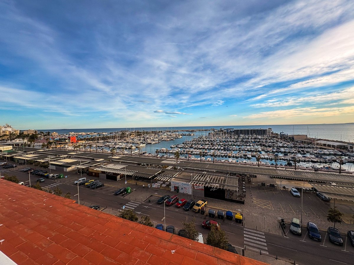 Rooftop view of a marina with boats and cityscape under a blue sky