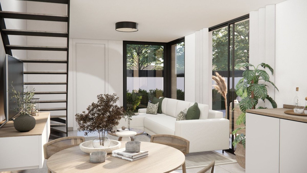 Modern living room with large windows, a white sectional sofa, dining table, and stairs. Lush greenery visible outside.