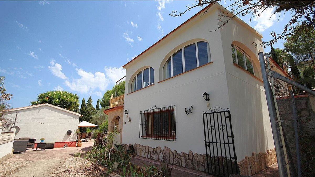 Exterior of a white villa with arched windows under a sunny blue sky, featuring a patio and garden.