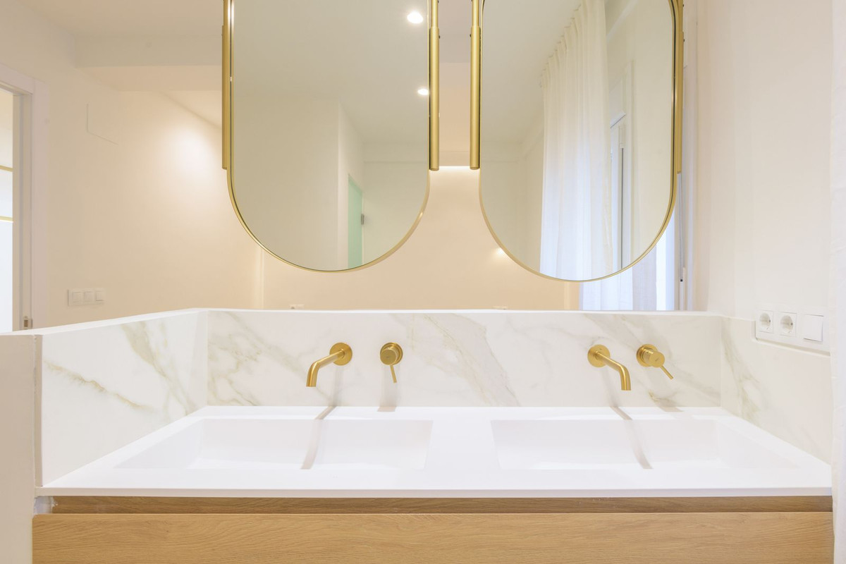 Moderne badkamer met dubbele wastafel en gouden details.