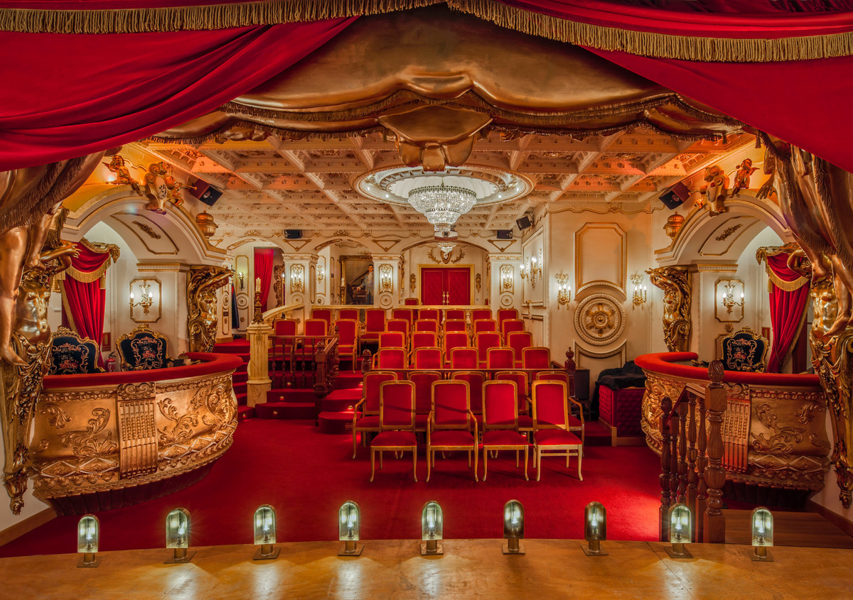 Luxe privé theaterzaal met rode stoelen en gouden accenten.