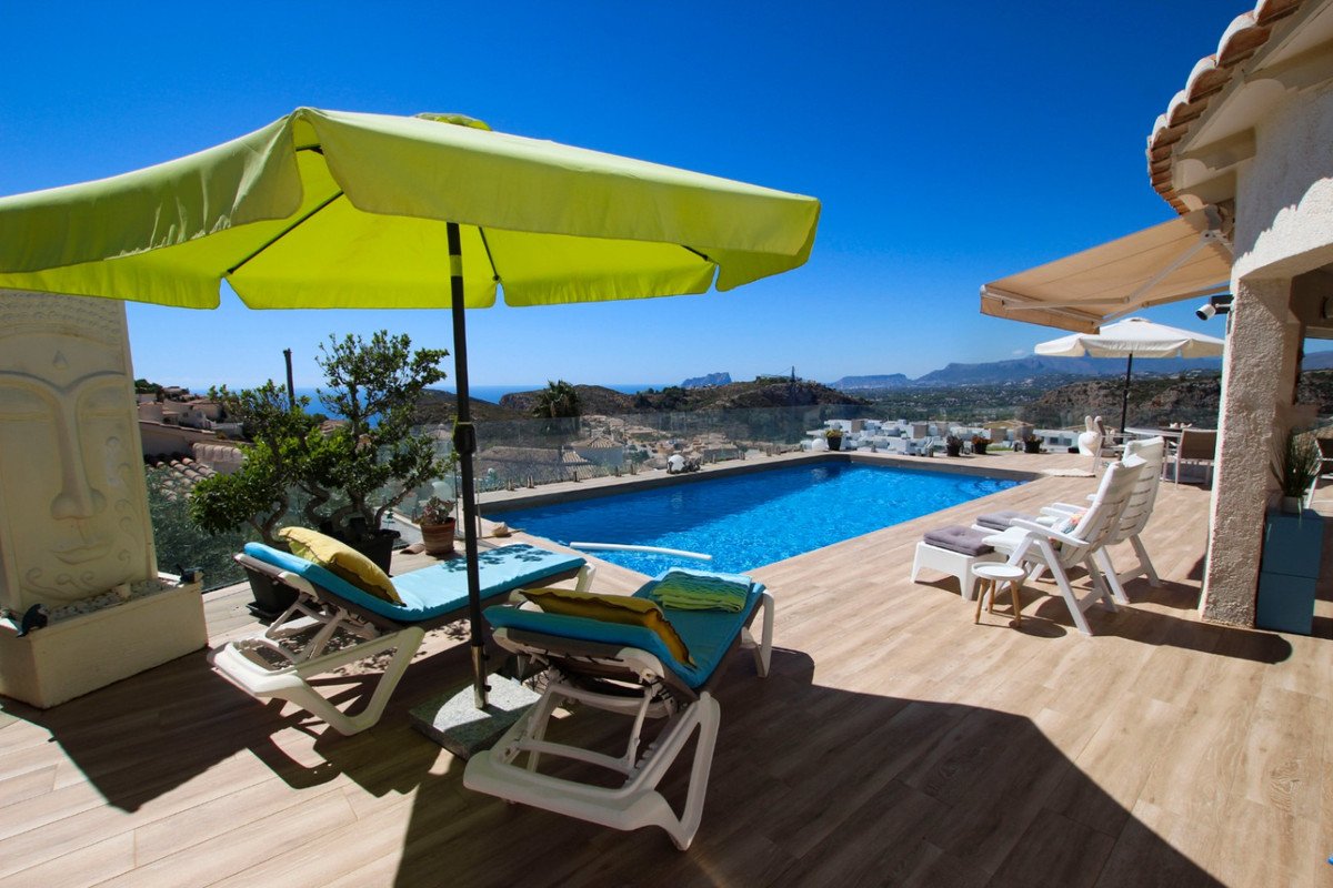 A luxury outdoor terrace with a swimming pool, sun loungers, and umbrellas, offering a stunning panoramic view of the sea and landscape.