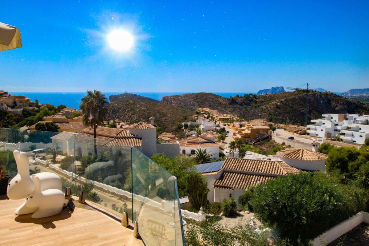 Modern villa terrace with a stunning panoramic view of the sea and surrounding hillside homes under a sunny sky.