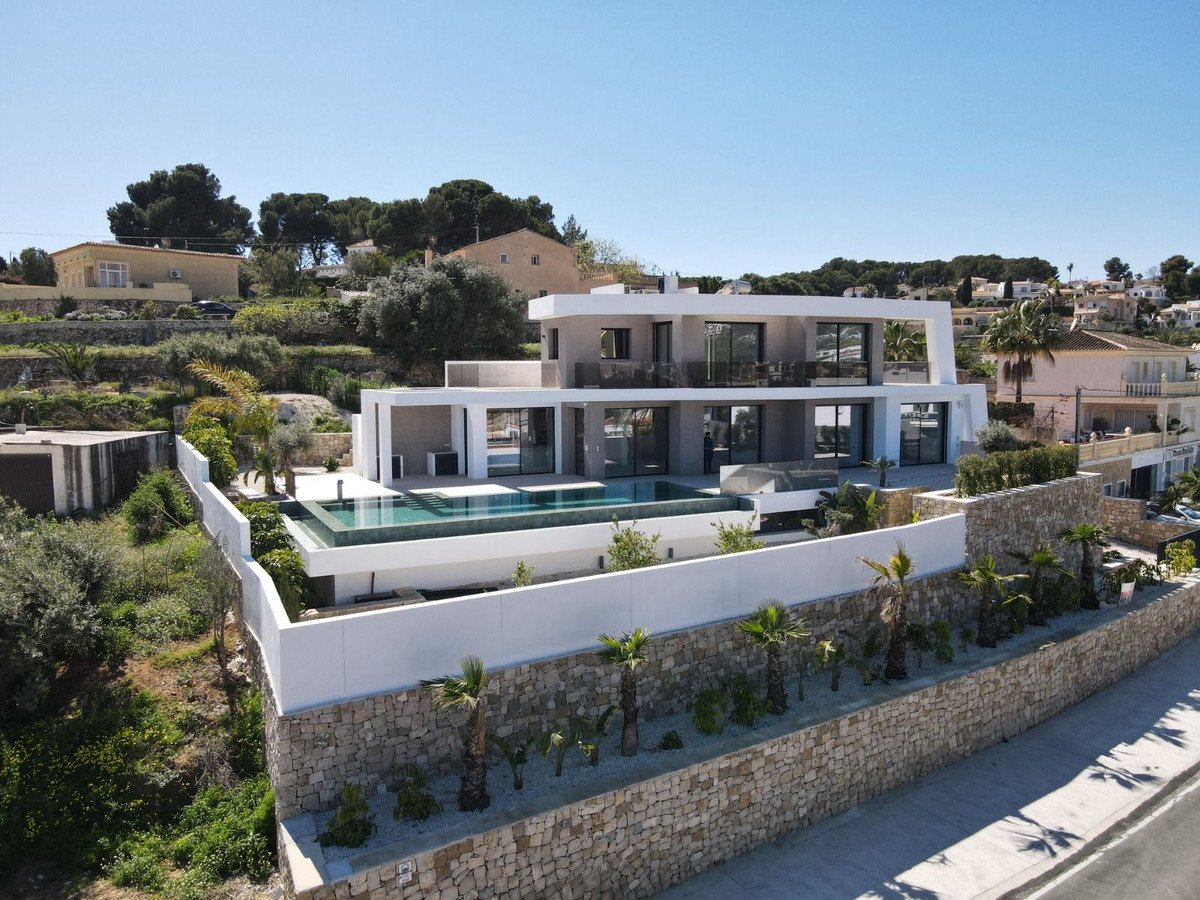 Modern villa with an infinity pool and ocean views, surrounded by lush greenery and palm trees. Sunny day.