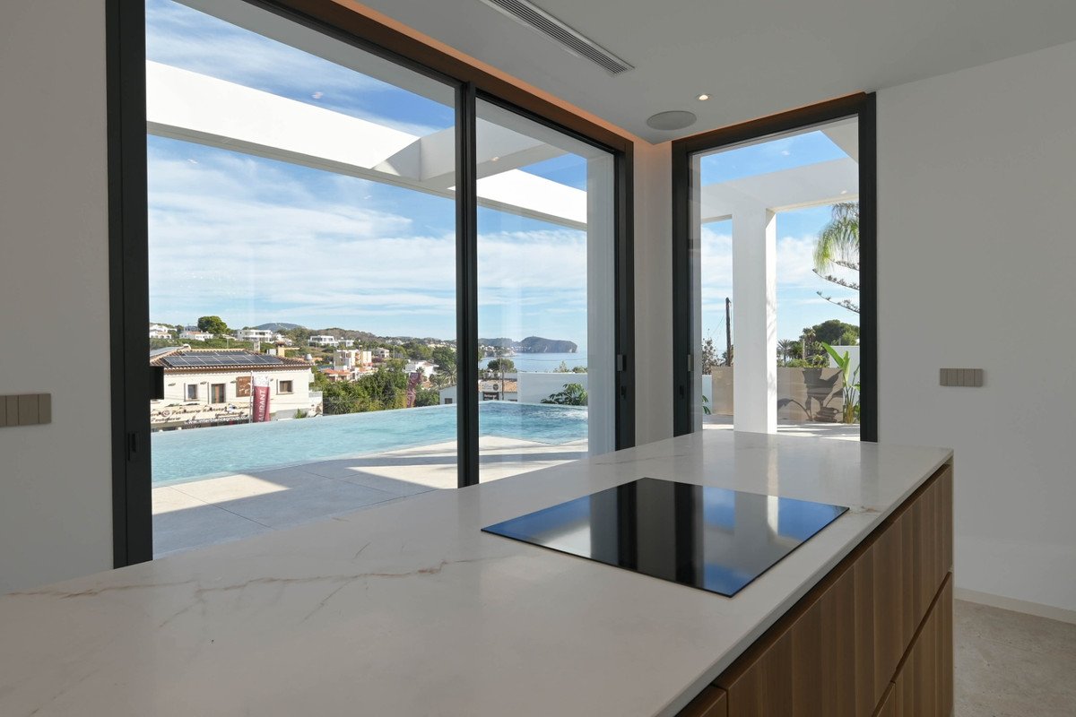 Modern kitchen island with induction hob overlooks an infinity pool and sea view through large glass doors.