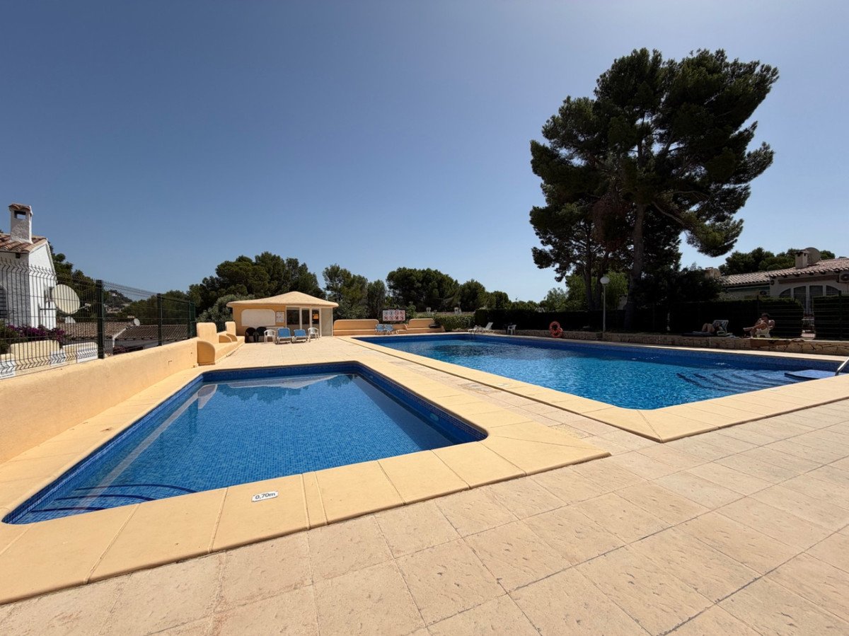 Two blue swimming pools with tiled surrounds and loungers on a sunny day, with trees and buildings in the background.