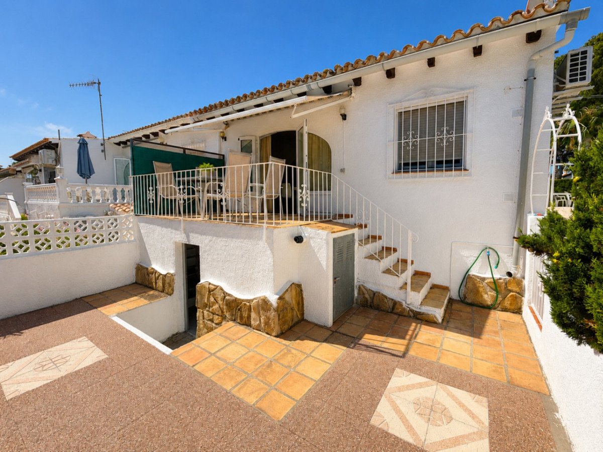 Terrace with outdoor seating and umbrella on a sunny day, with stairs leading down to a paved patio area.