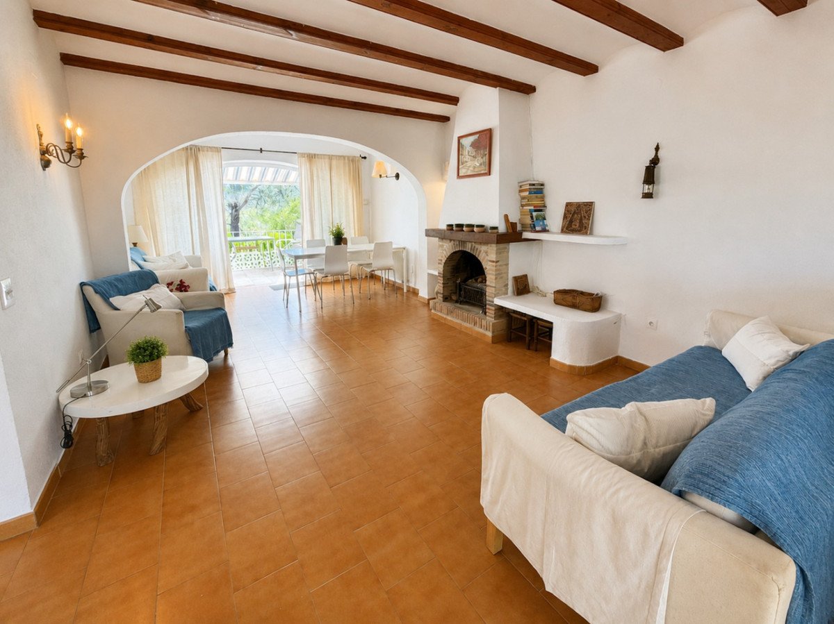 Spacious living and dining area with a fireplace, arched doorway leading to a terrace with outdoor seating and green views.