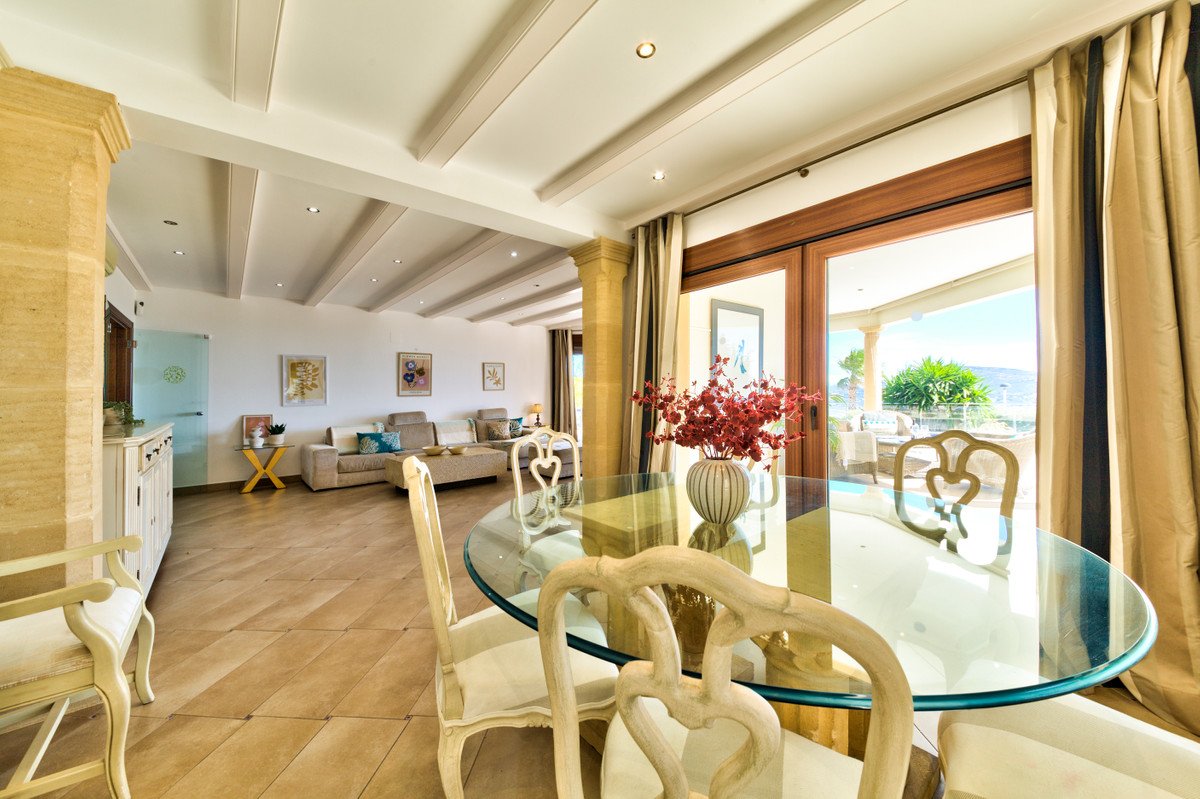 Spacious dining and living area with a glass table, elegant chairs, and a balcony offering a sea view.
