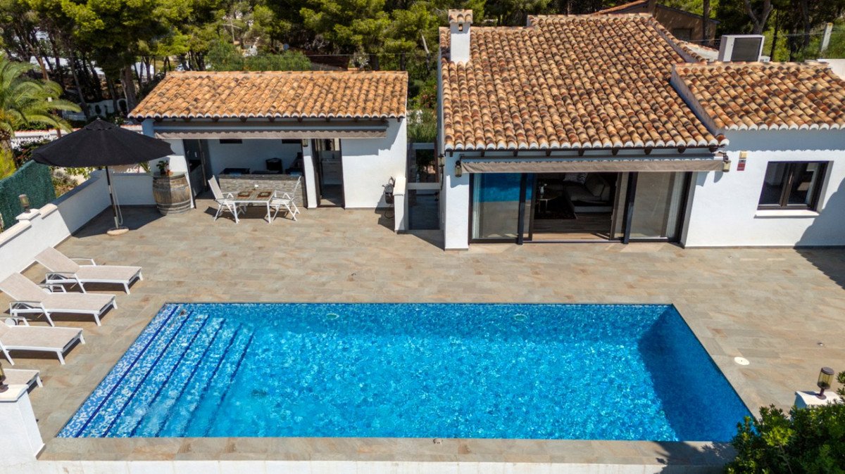 Luxury villa with a swimming pool, outdoor kitchen area, lounge chairs, and covered dining space under a blue sky.