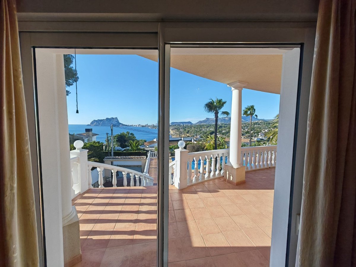 Balcony with a view of the sea, pool, and palm trees, accessible through sliding glass doors.