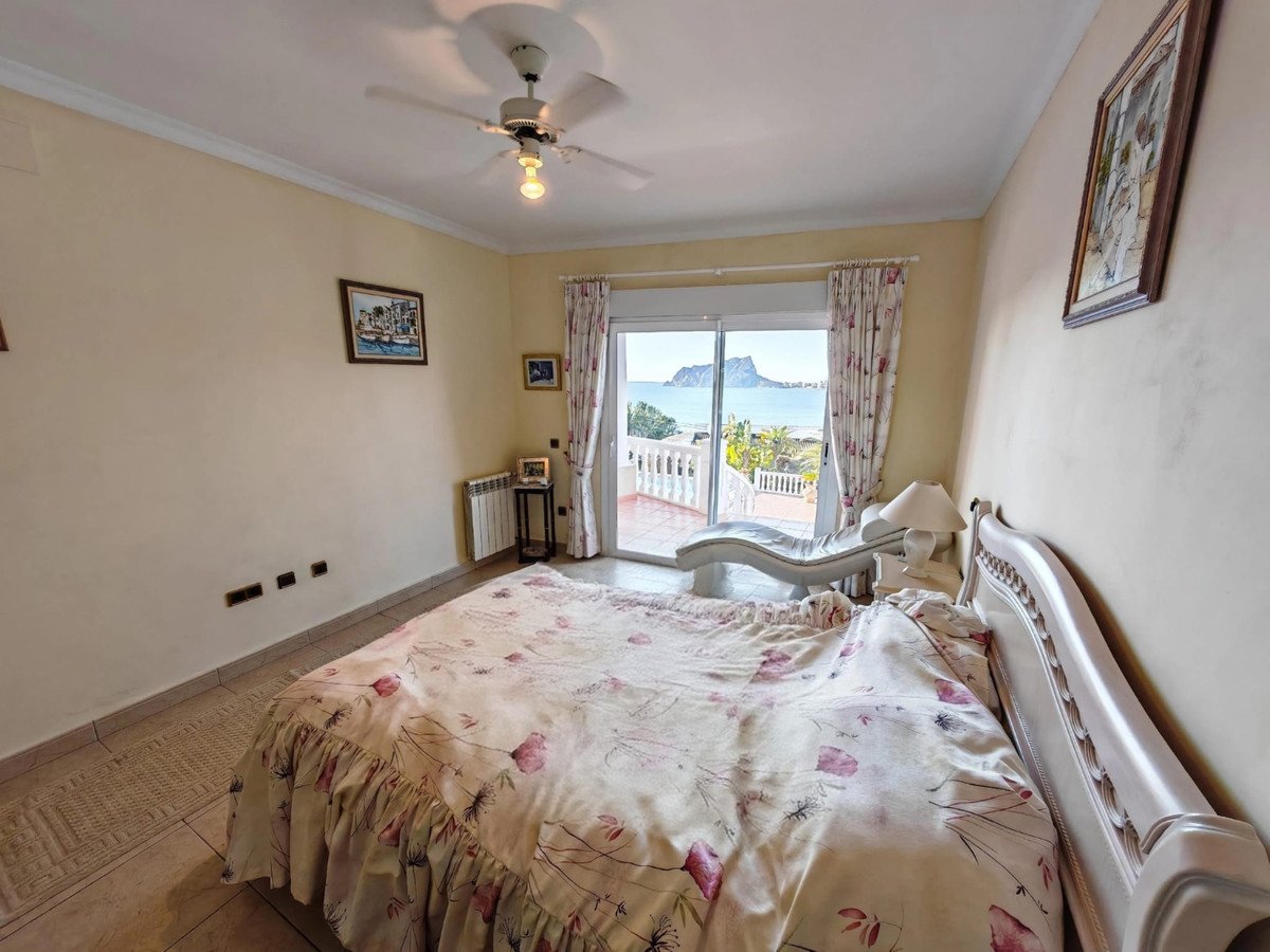 Bedroom with a bed, chaise lounge, and balcony doors opening to a beautiful sea view and distant mountains.