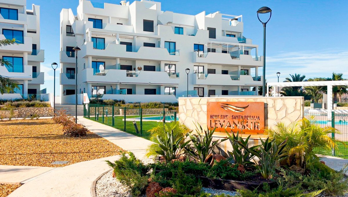 Modern apartment buildings with balconies, a swimming pool, and manicured landscaping with a prominent development sign.