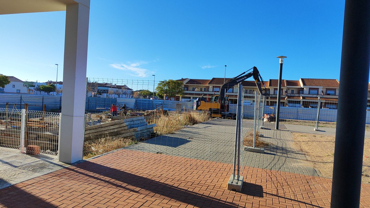Construction site with crane, brick pavement, and residential buildings in the background.