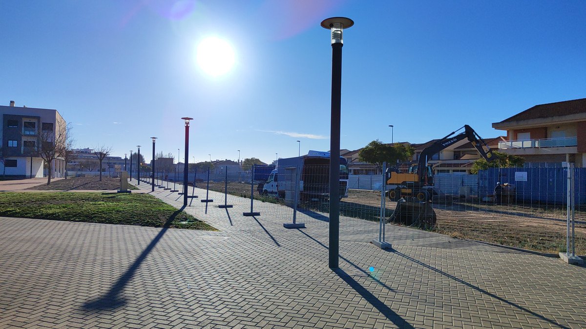 Construction site with cranes, paved walkway, and clear blue sky.