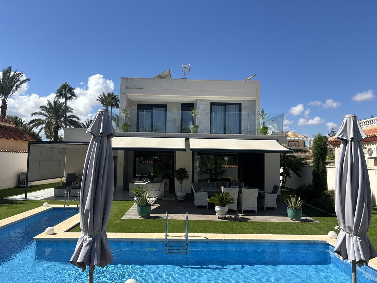 Modern villa with swimming pool, patio furniture, and tropical plants under a clear blue sky.
