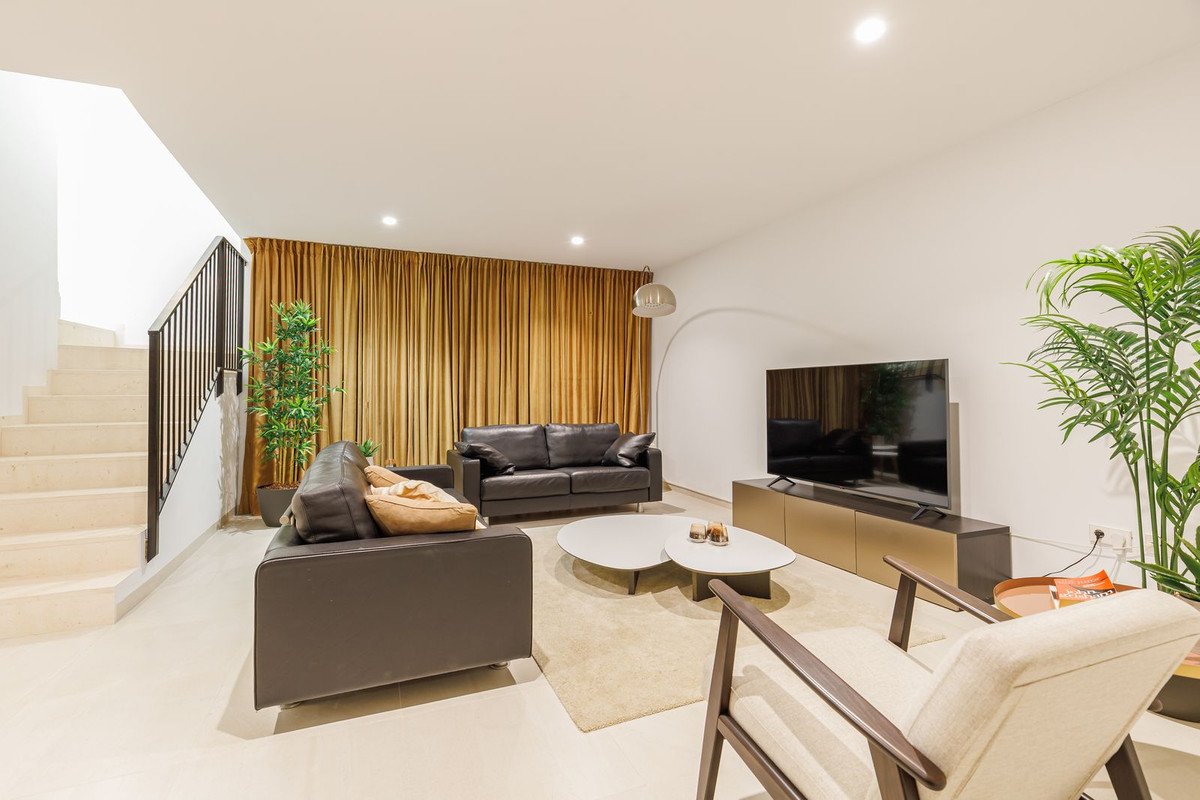 A modern living room features a dark leather sofa, armchair, coffee table, and a large TV mounted on a console.