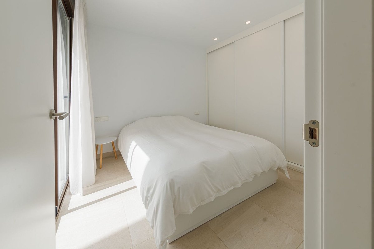 Bright bedroom with a white duvet-covered bed, modern sliding door closet, and a balcony door with sheer curtains.