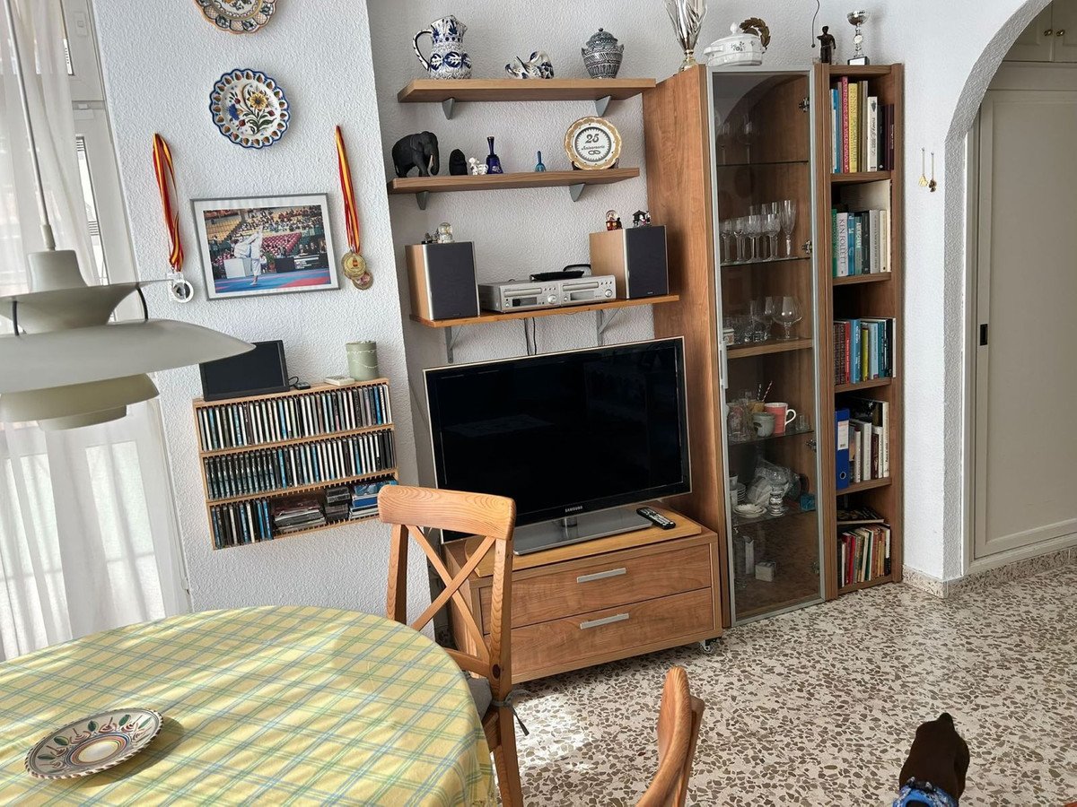 Living room with a television, display cabinet with glasses, and shelves filled with books and decorations.