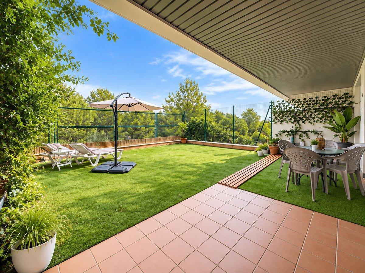 Spacious terrace with artificial grass, lounge chairs, an umbrella, and a dining set overlooking a lush green landscape.