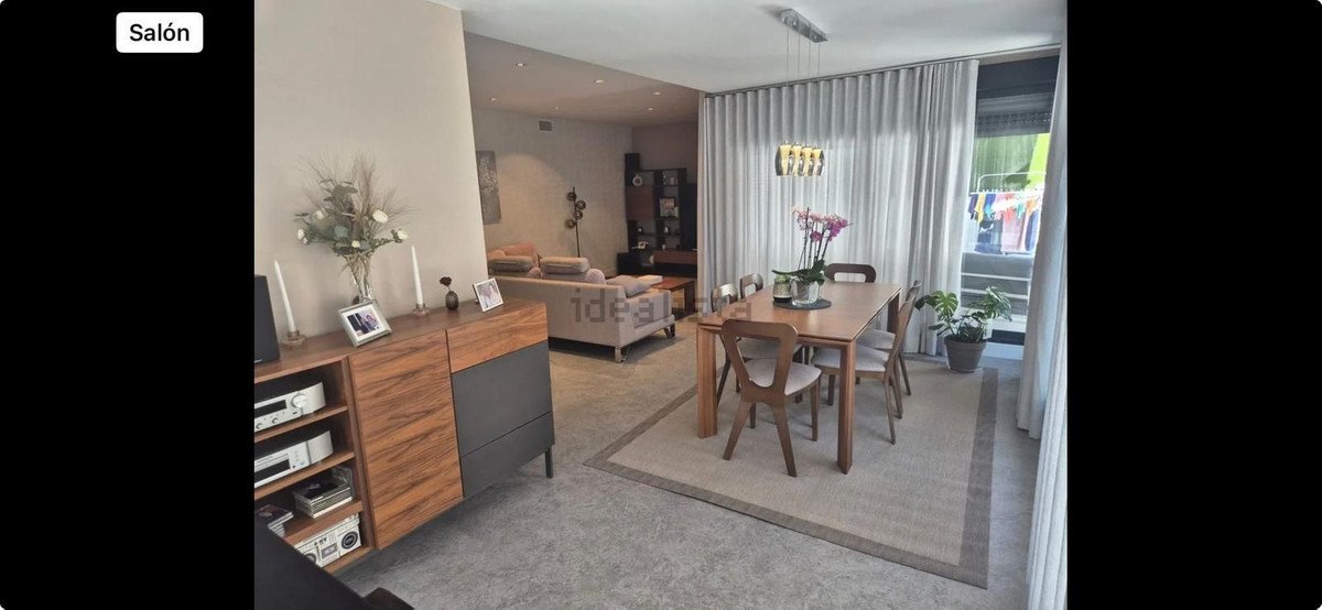 A modern living and dining area with a wooden table, chairs, sofa, and a large window with curtains.