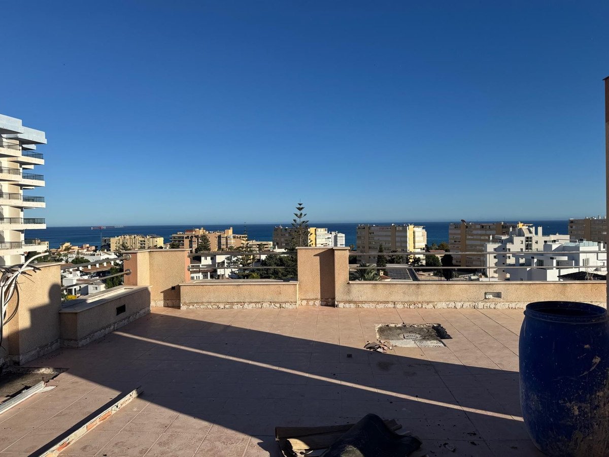 A wide view from a terrace overlooking a town and the sea under a clear blue sky.