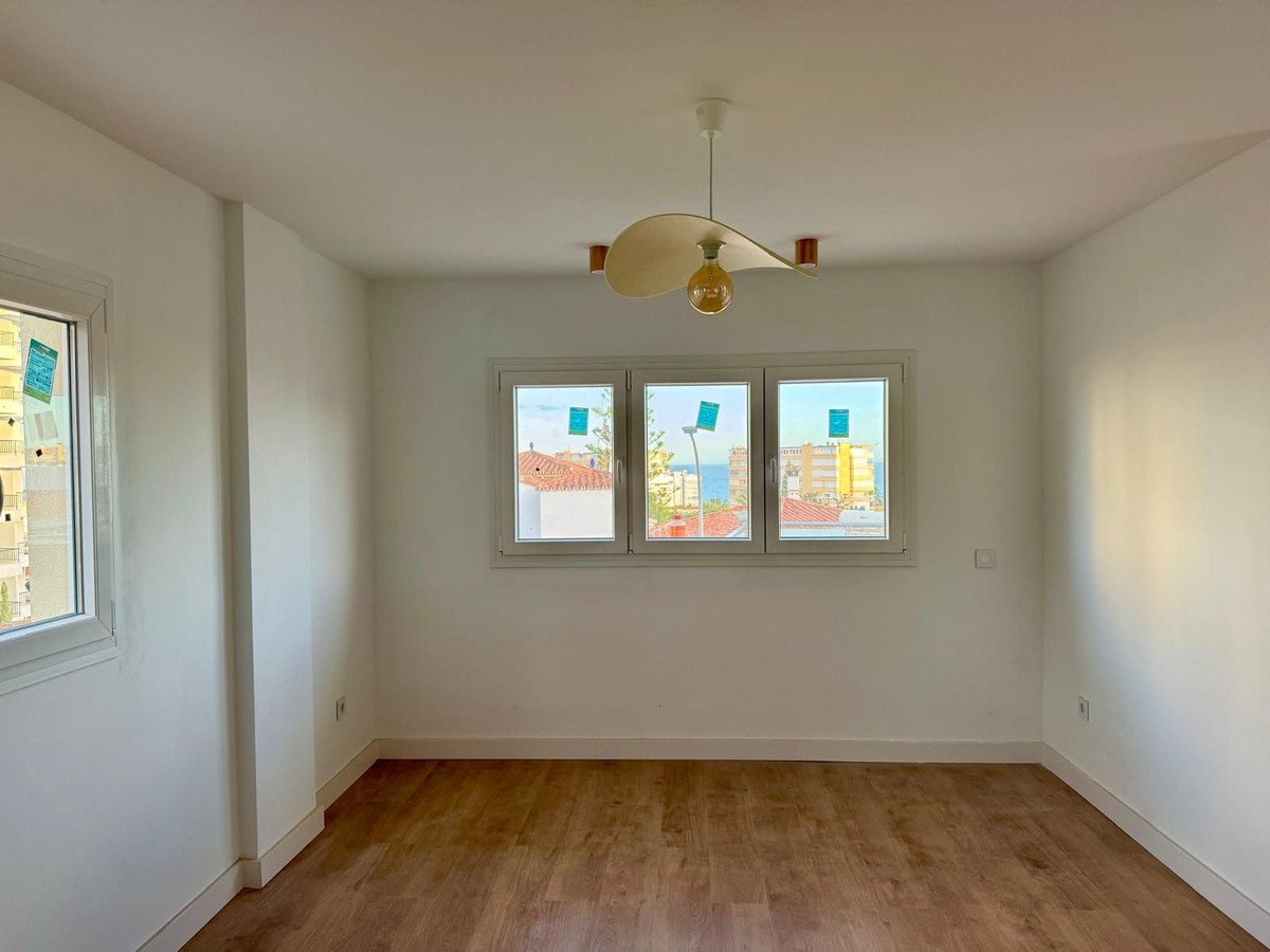 Empty living room with large windows offering a view of the ocean and cityscape. Modern lamp on ceiling.