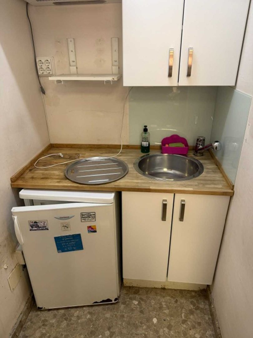 Compact kitchenette with a sink, countertop, cabinets, and a small refrigerator below.