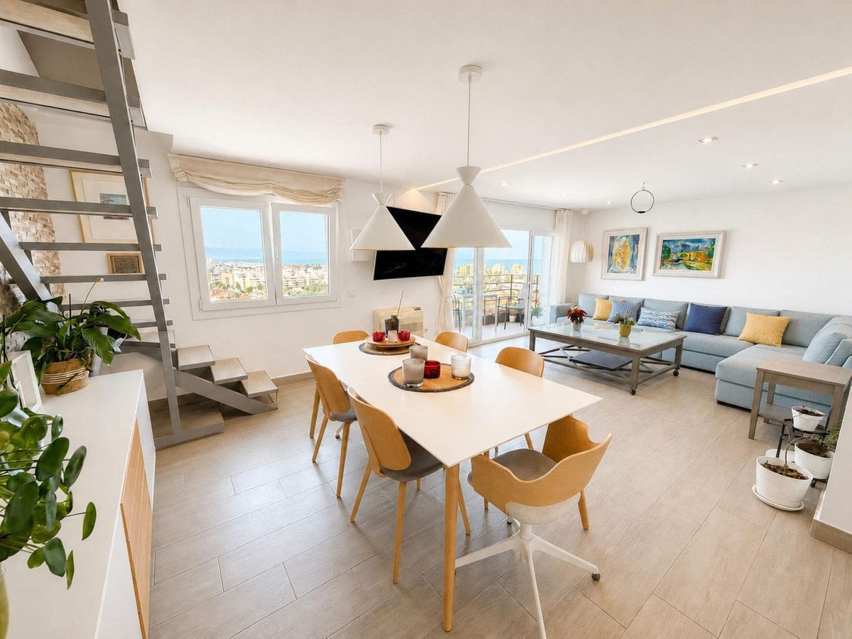 Modern open-plan living space with dining table, sofa, and sea view through large windows.