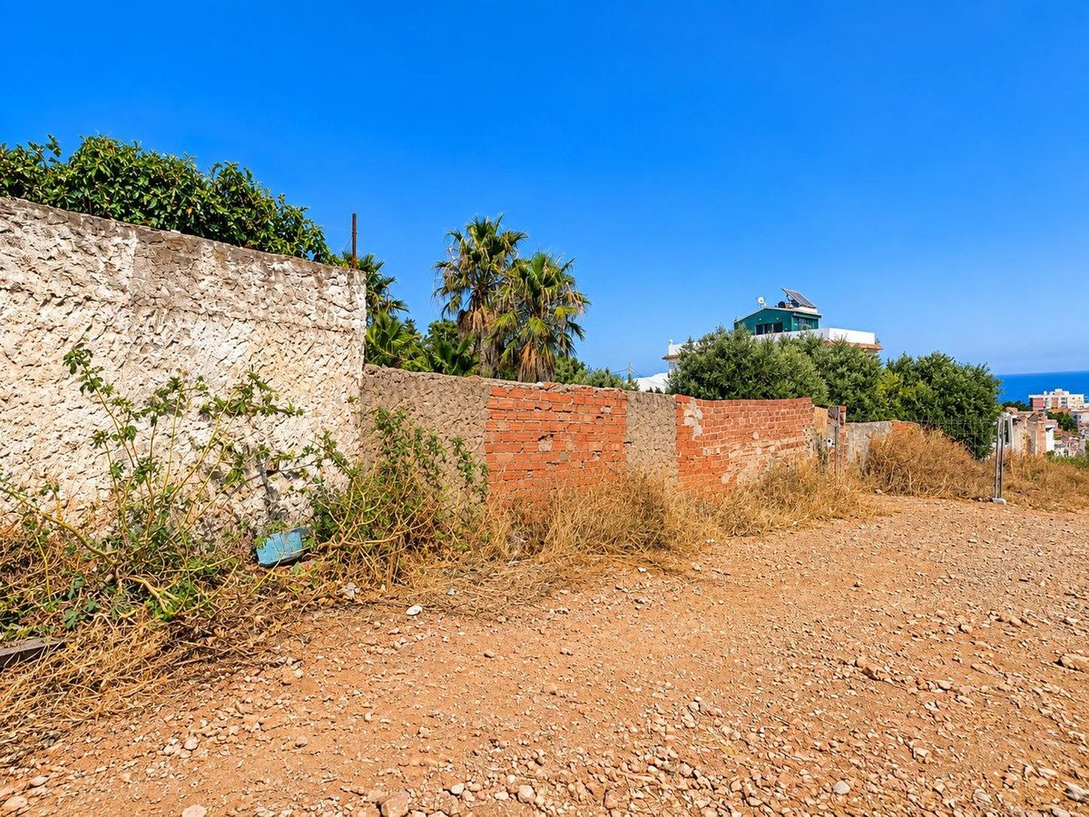 Rural plot of land with stone and brick walls, overlooking a coastal town with palm trees and blue sky.