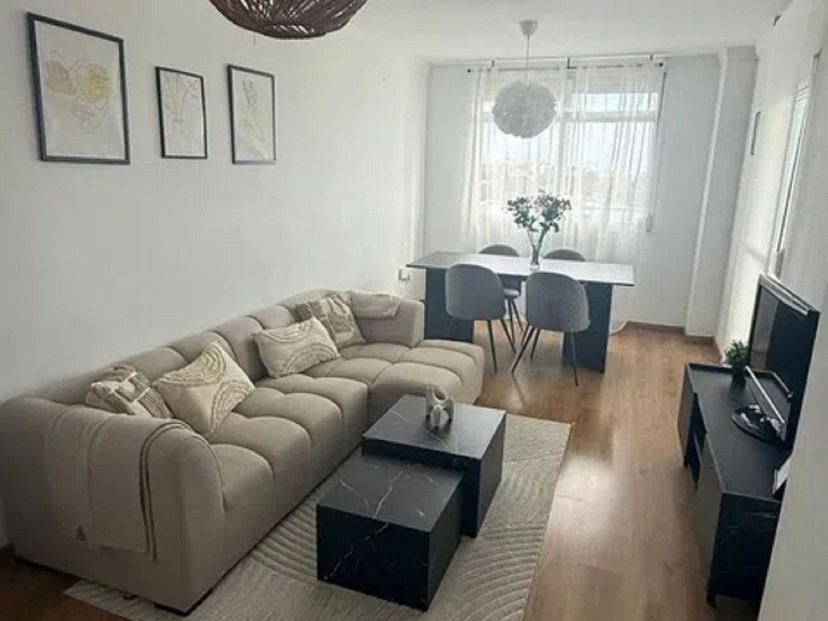 A modern living and dining area with a sectional sofa, coffee table, dining set, and TV stand against a window with sheer curtains.