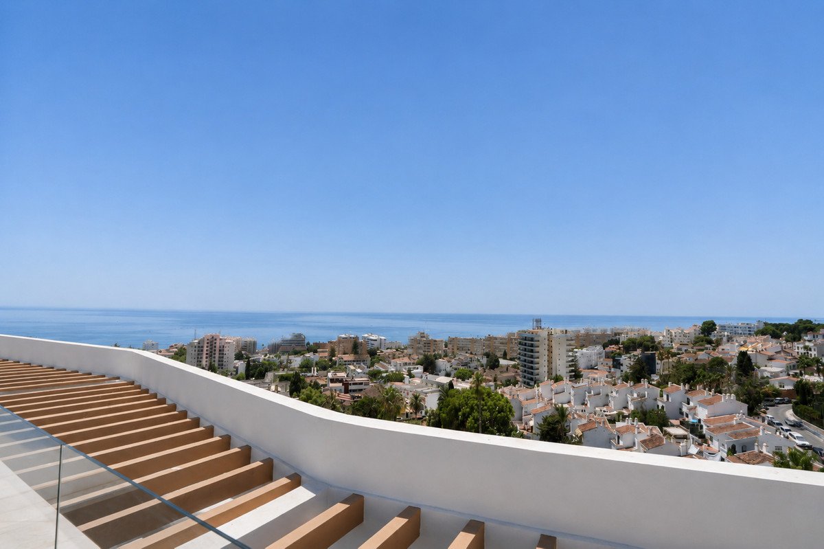 A panoramic view from a modern terrace overlooking a coastal town and the blue sea on a clear day.