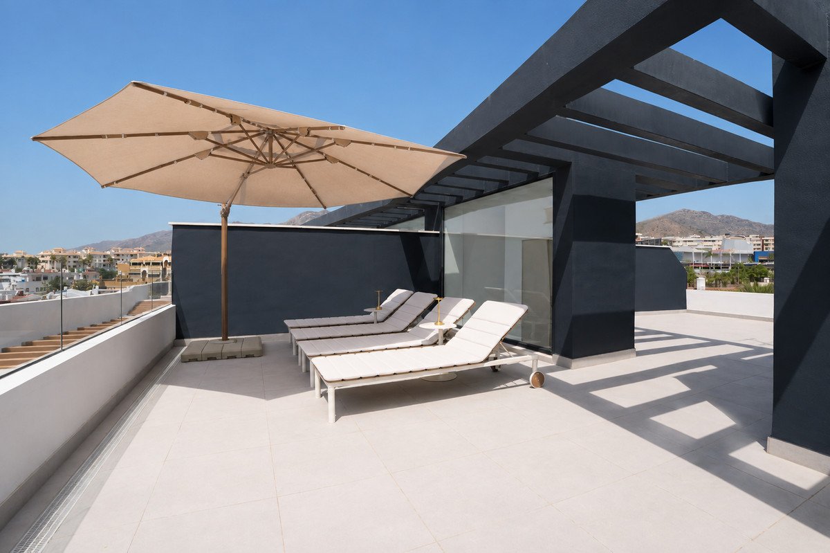 Spacious terrace with lounge chairs and umbrella, offering a view of the distant town and hills under a clear blue sky.