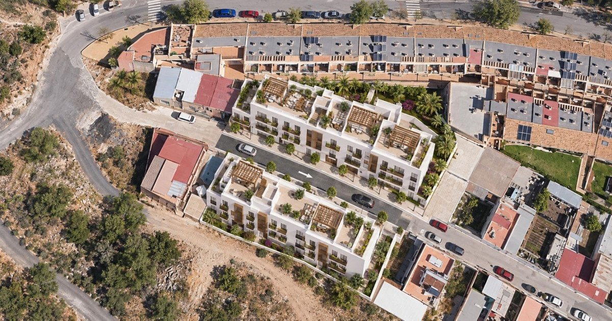 Aerial view of modern white apartment buildings with rooftop terraces, surrounded by trees and a road.