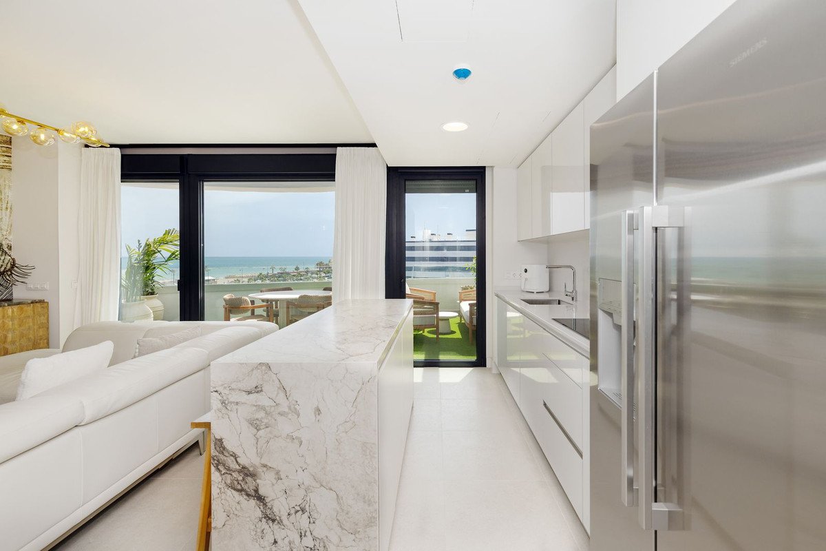 Modern kitchen and living area with a marble island and a balcony overlooking the sea and a table.