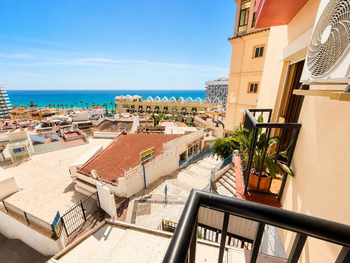 Balcony with sea view overlooking a town with buildings and the ocean under a clear blue sky.