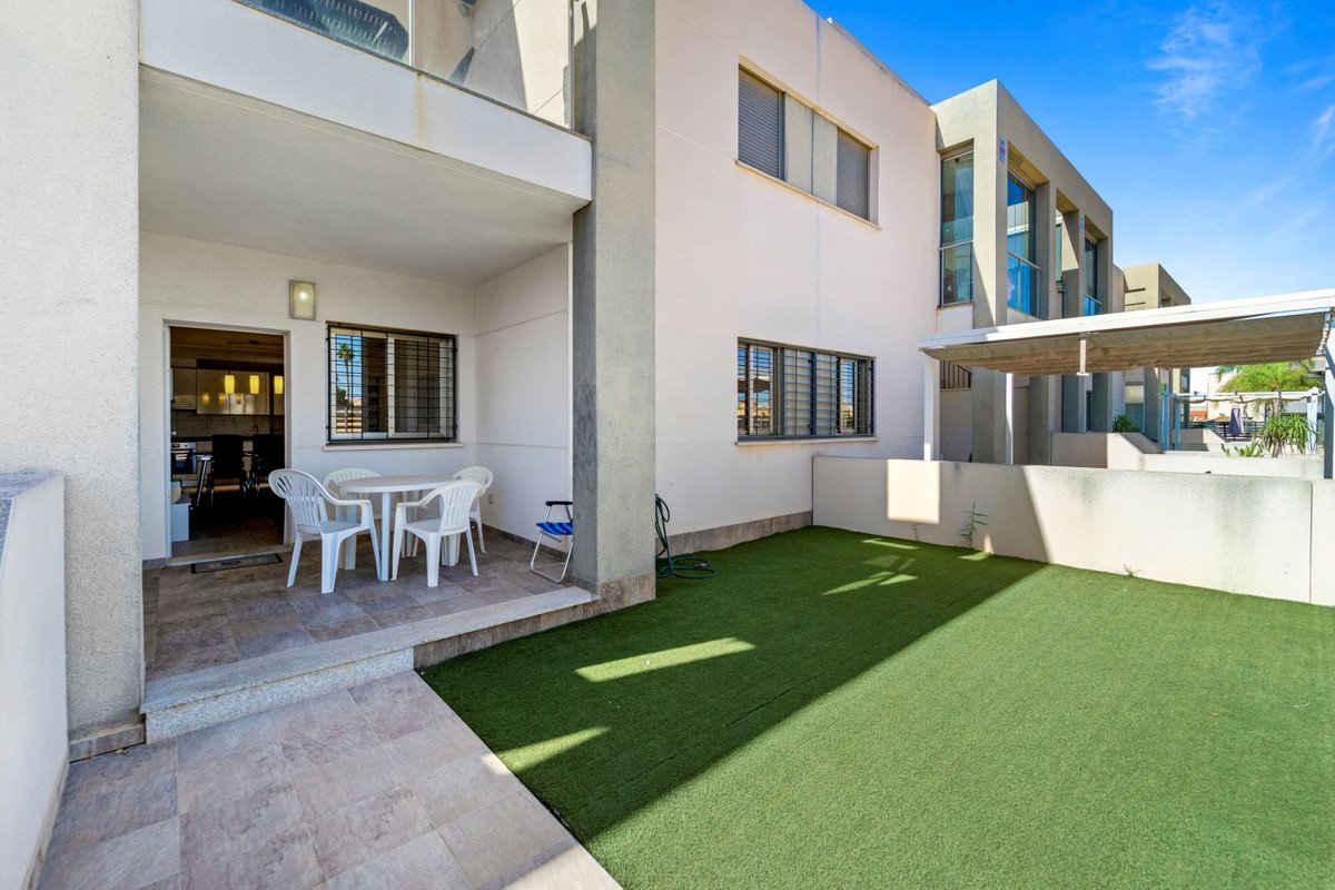 A covered terrace with a table and chairs, adjacent to a small lawn area. Leads into a kitchen.