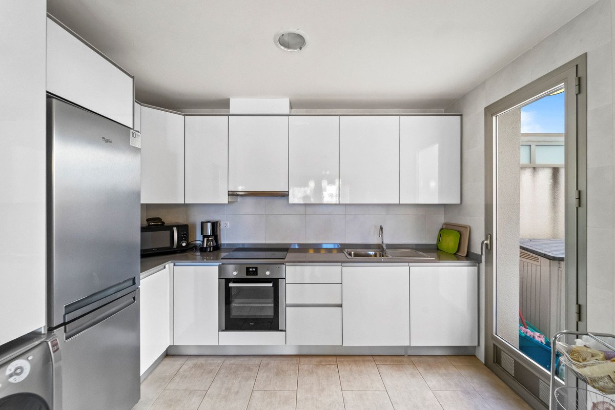 Modern white kitchen with stainless steel appliances, sink, stove, microwave, and a door leading outdoors.