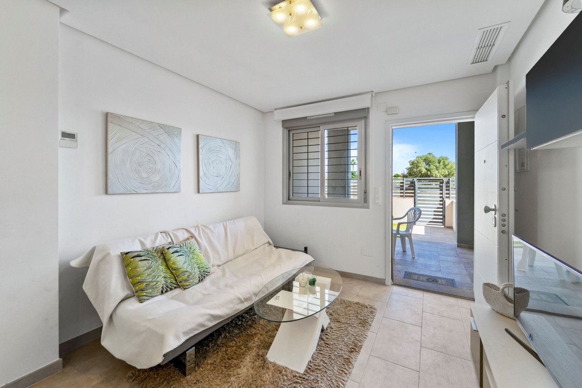 A bright living area with a sofa, coffee table, and a view of a sunny terrace with a chair through an open door.