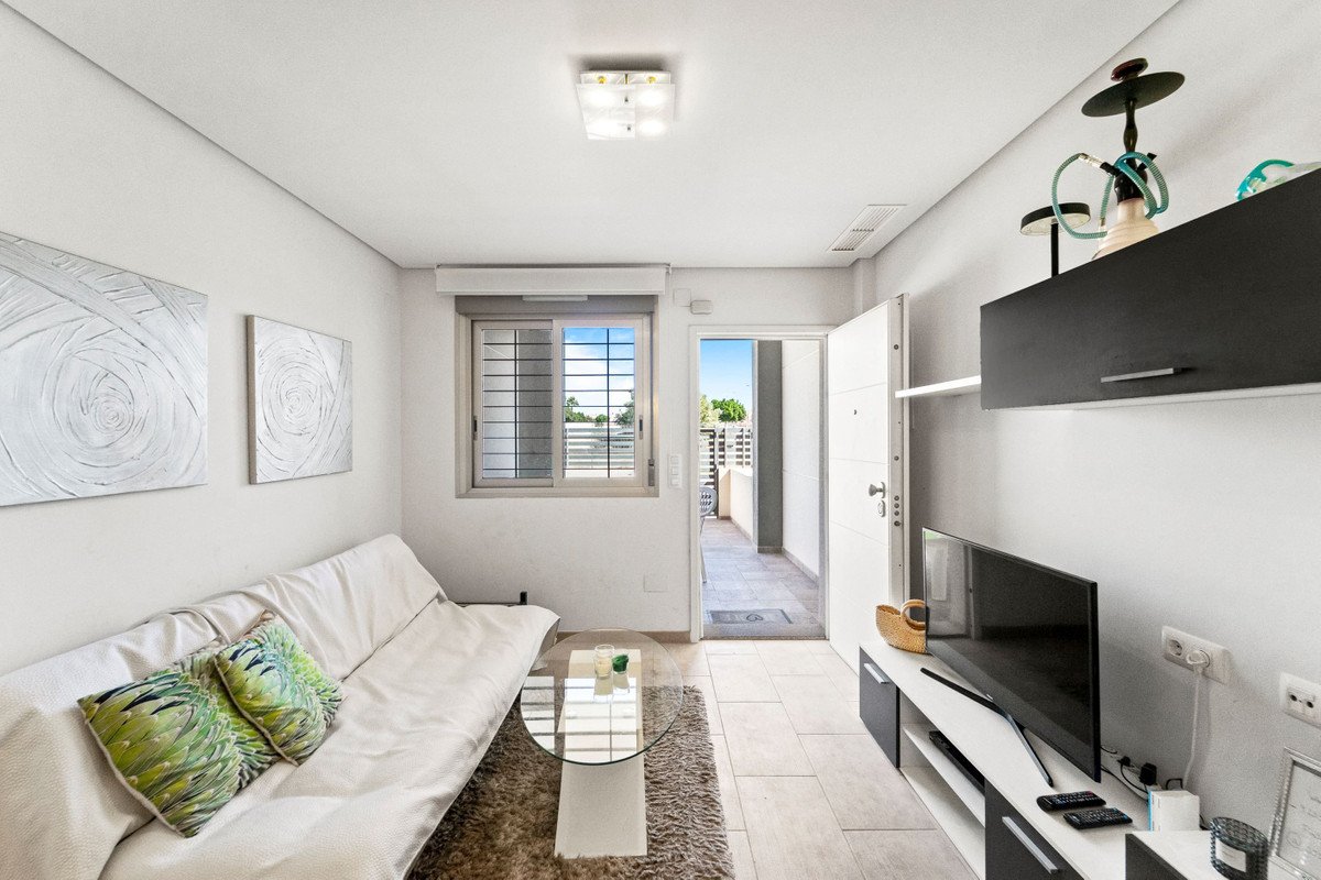 Living room with sofa, coffee table, and TV, opening onto a balcony with a bright view.