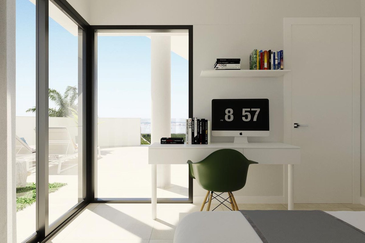 Modern home office with a white desk, green chair, computer, and large sliding glass doors revealing a sunny terrace and sea view.