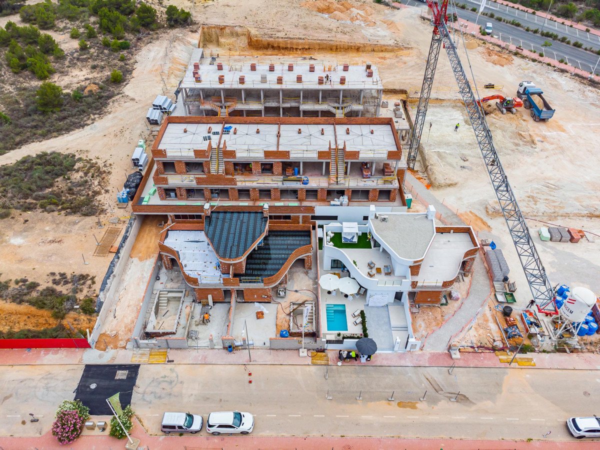 Aerial view of a modern villa complex under construction, featuring a swimming pool and outdoor seating area. Construction cranes are visible.