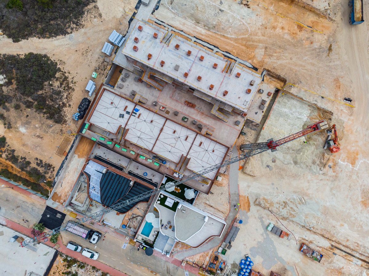 Aerial view of a construction site with buildings, a crane, and a swimming pool area.