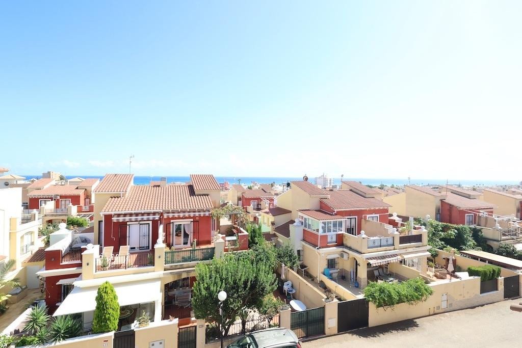 View over a row of townhouses with terracotta roofs towards the blue sea and sky on a sunny day.