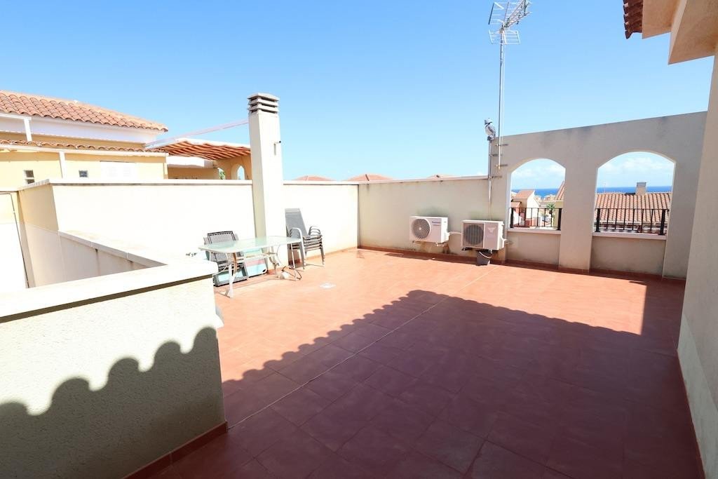 Spacious tiled terrace with table and chairs, air conditioning units, and a distant view of the sea under a clear blue sky.