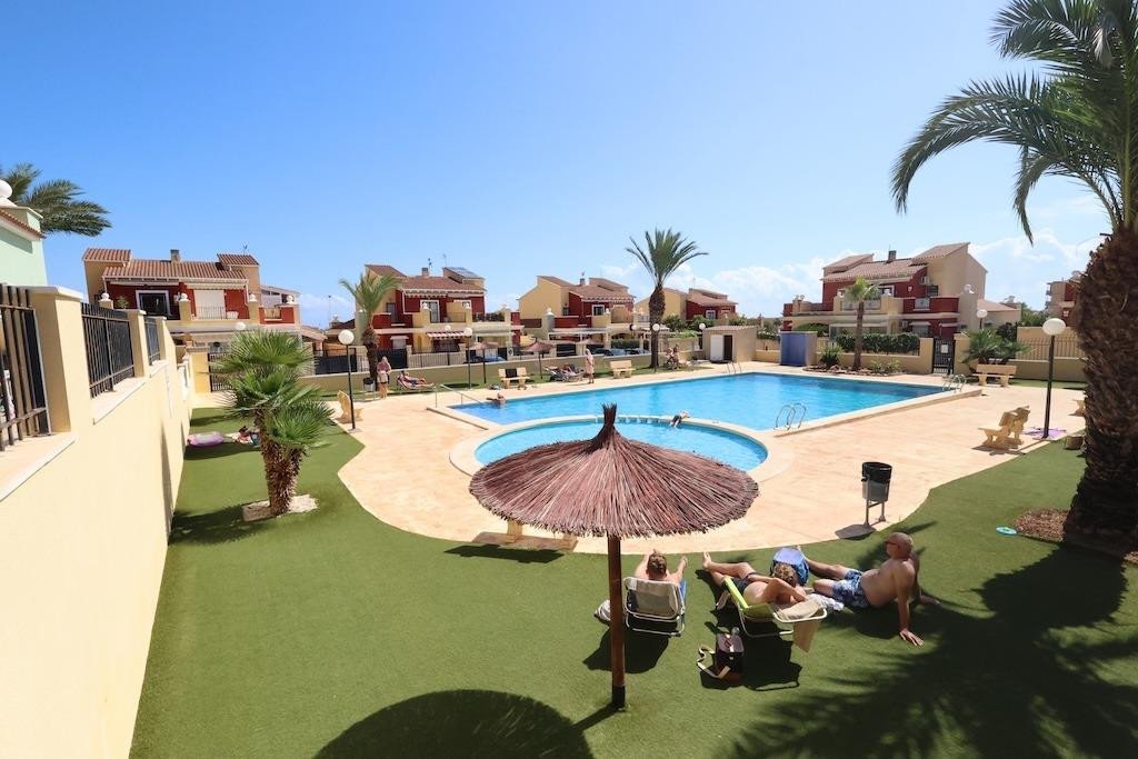 People relax by a large communal pool and patio area, surrounded by palm trees and residential buildings.