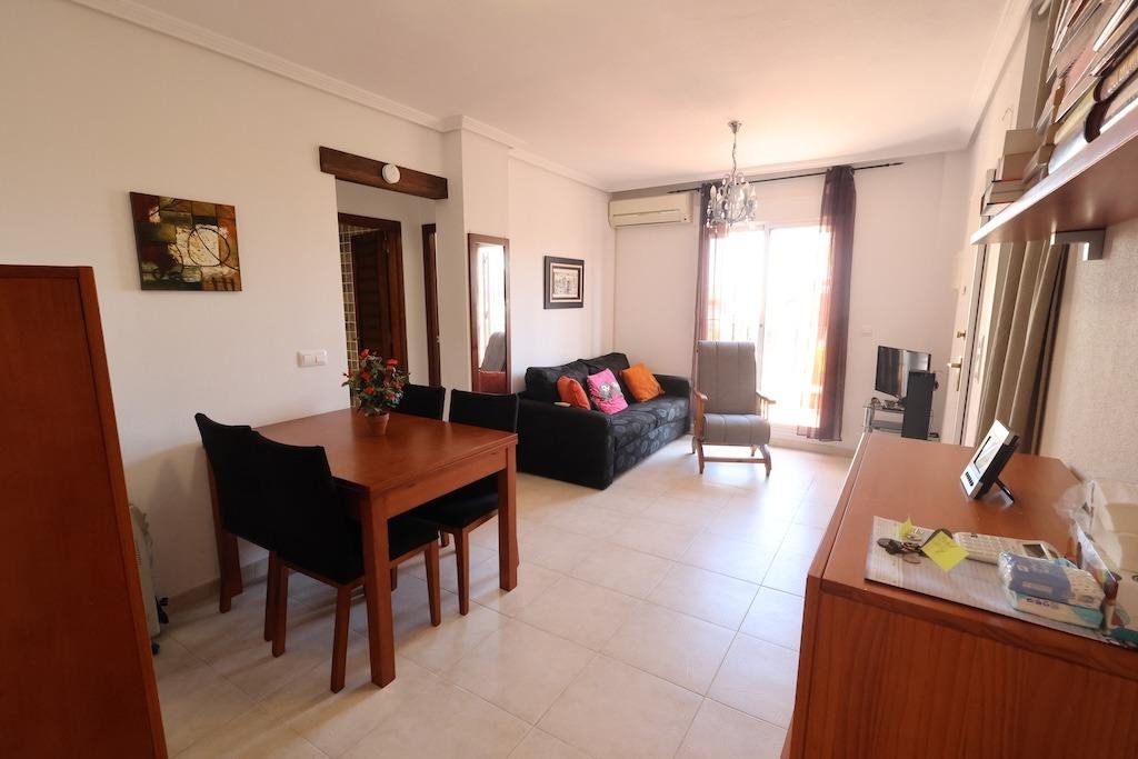 Bright living and dining room with a sofa, armchairs, a dining table, and large windows letting in natural light.